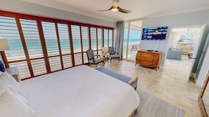 Une chambre d’hôtel avec un grand lit, une télévision, une commode en bois et un balcon avec vue sur la mer.