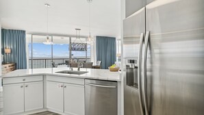 A modern kitchen with stainless steel appliances, a large island with a sink, and a view of the outdoors through large windows.