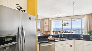 A modern kitchen with a stainless steel refrigerator, a built-in water dispenser, and a large window offering a view of the ocean.