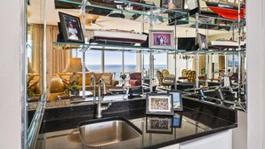 A modern kitchen with a black countertop, stainless steel sink, and glass shelving displaying various items.