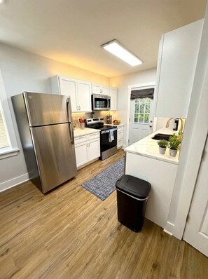 A modern kitchen with white cabinets, stainless steel appliances, and a small island with a sink. - Cozy unit, King bed & laundry (Wilmington)