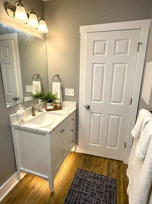 A bathroom with a white vanity, a mirror, a sink, and a door. - Cozy unit, King bed & laundry (Wilmington)