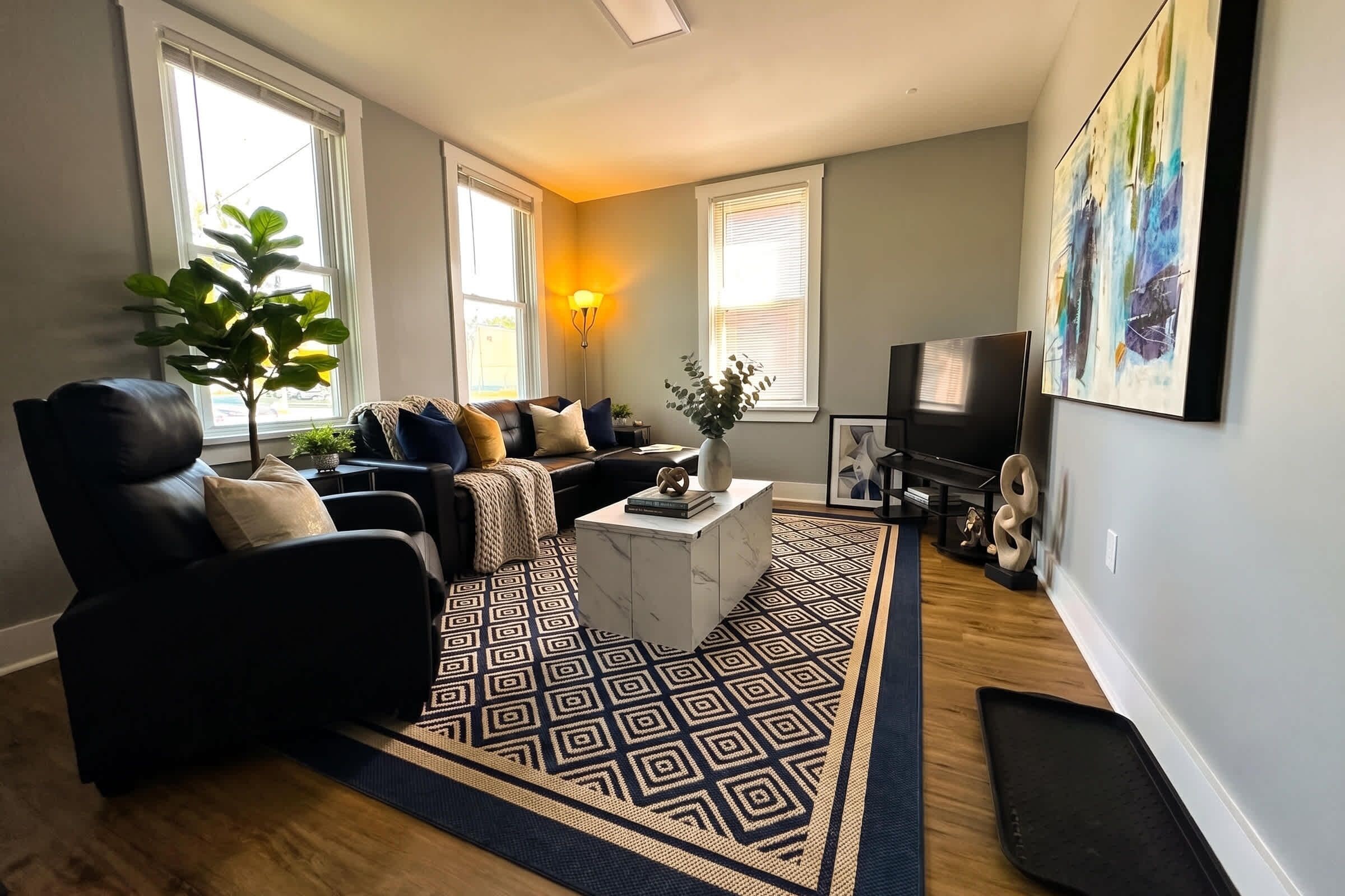 Living room with sofa seating, TV, coffee table, large windows, and wall art.