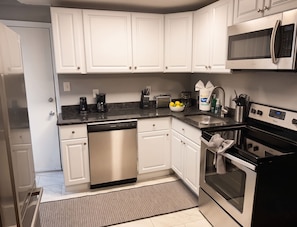 A modern kitchen with white cabinetry, a dishwasher, a microwave, a toaster, and a sink. - Spacious Historic King Suite (Wilmington)