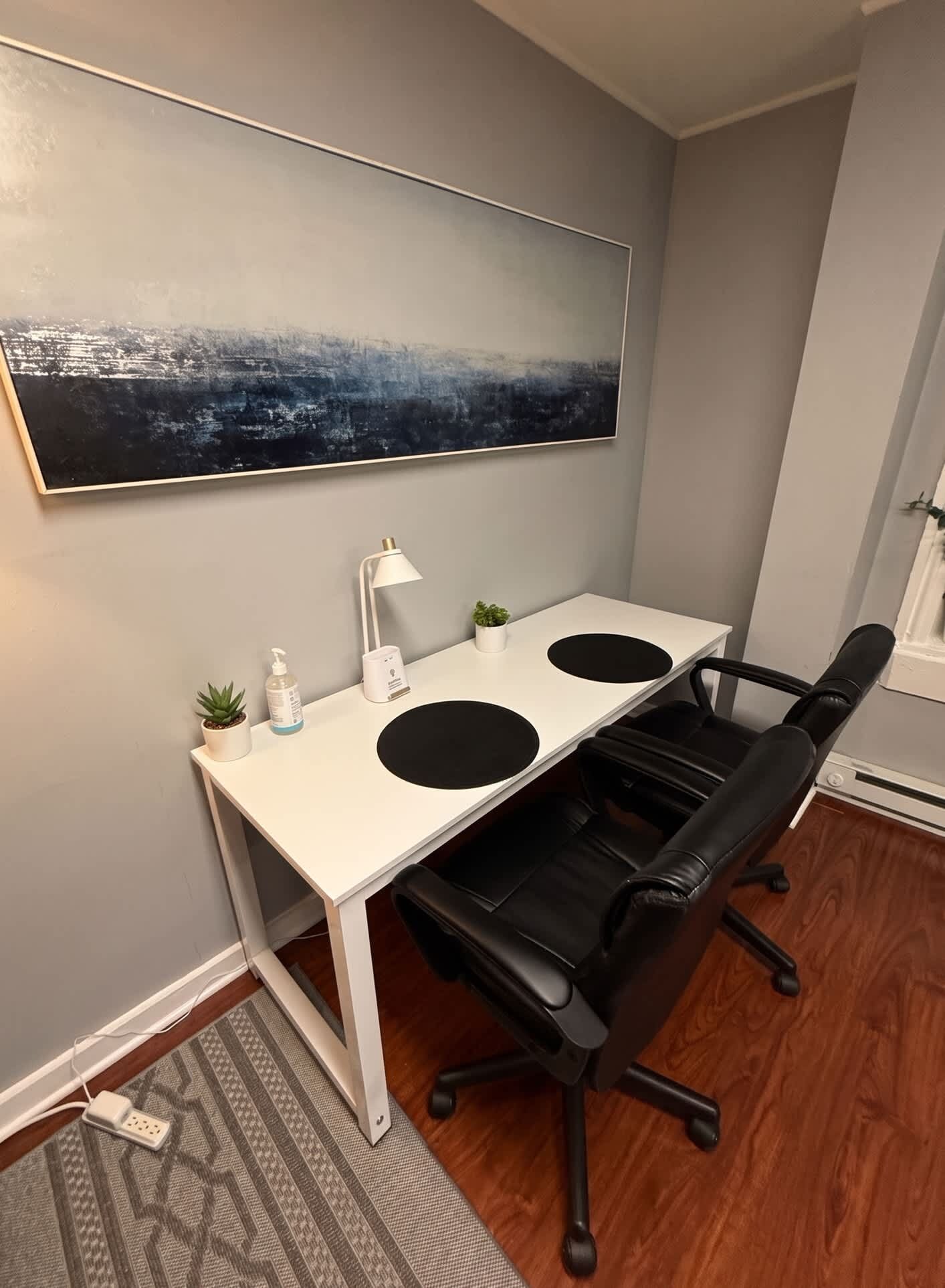 Un espacio de oficina moderno con un escritorio blanco, una silla de oficina negra y un cuadro abstracto grande en la pared.
