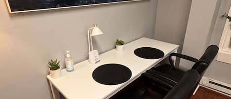 Un espacio de oficina moderno con un escritorio blanco, una silla de oficina negra y un cuadro abstracto grande en la pared.
