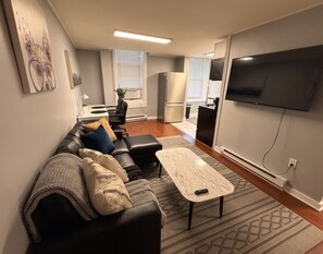 A modern living room with a black leather sofa, a marble coffee table, and a flat-screen TV mounted on the wall. - Spacious Historic King Suite (Wilmington)