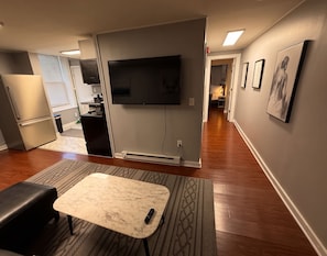 A modern living room with a flat-screen TV, a marble coffee table, and a black bench.