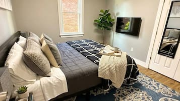 Une chambre à coucher avec un lit, une table de chevet, une lampe, une plante en pot et un téléviseur.