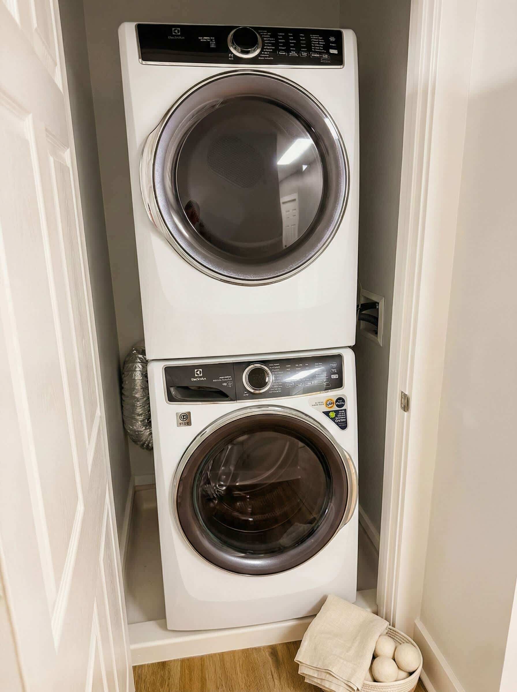 Un appareil compact combinant lave-linge et sèche-linge, à deux portes, installé dans un couloir étroit.