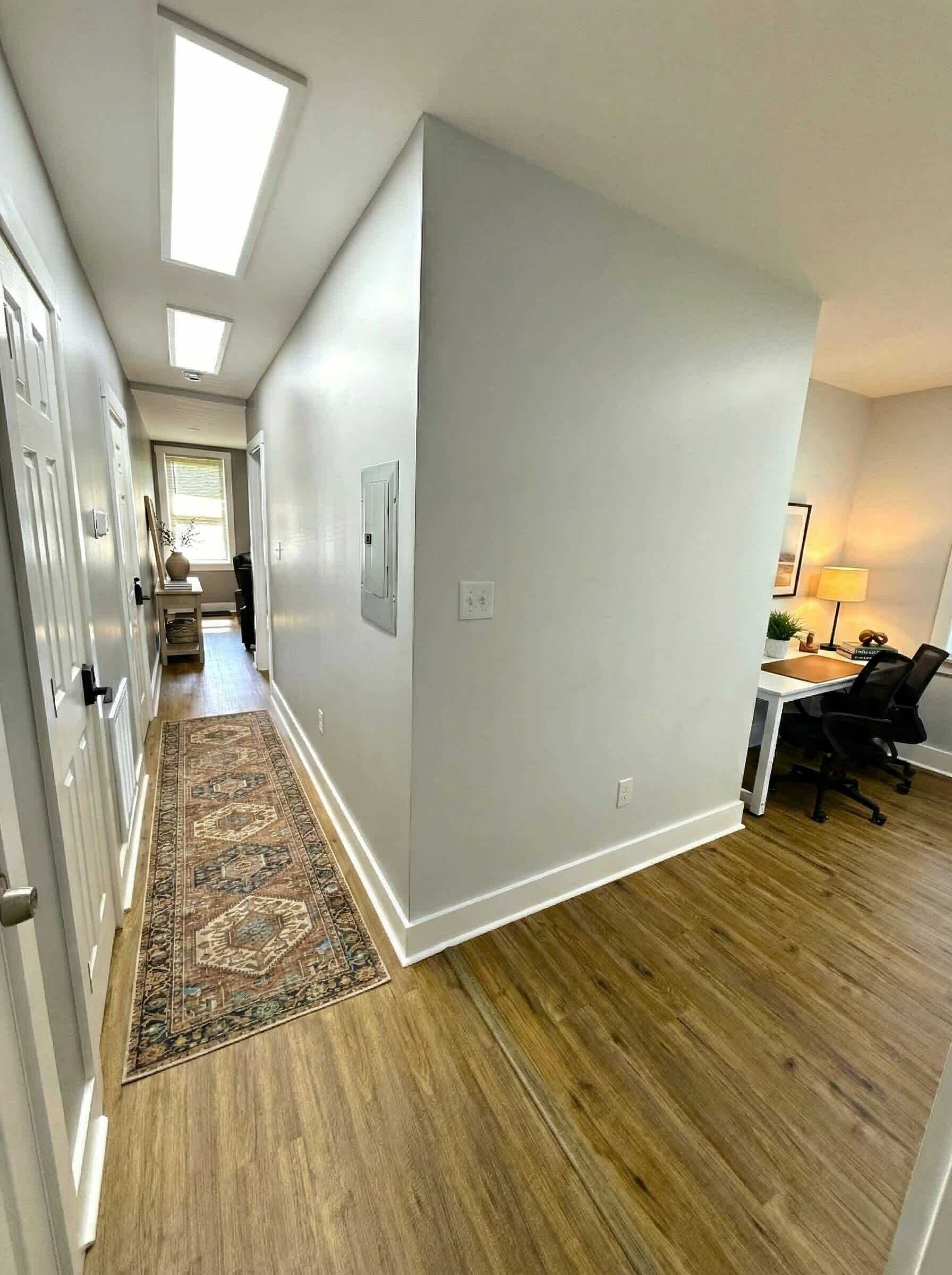 Un couloir doté d’un plancher en bois, d’un tapis à motifs et d’un bureau avec une chaise.
