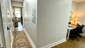 Un pasillo con piso de madera, alfombra estampada y un escritorio con silla.
