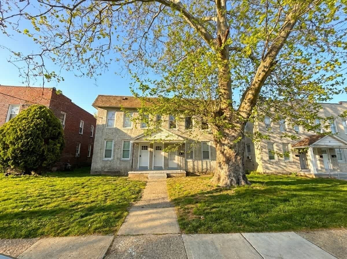 Une maison à deux étages avec un porche à l’avant, un grand arbre dans le jardin et une pelouse bien entretenue.