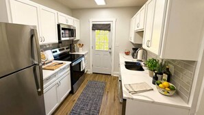 Una cocina compacta con armarios blancos, un refrigerador de acero inoxidable, un microondas y una estufa.