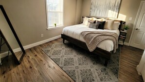 A bedroom with a bed, a window, a painting, and a door. - Modern Loft with Skyline Views - King & Queen Beds, Close to Downtown! (Wilmington)