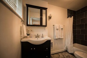 Une salle de bain avec un lavabo blanc, un meuble-lavabo foncé, un miroir, un rideau de douche et une baignoire.