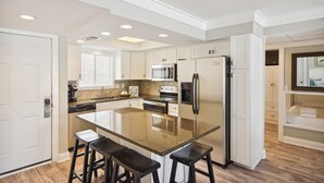 Une cuisine moderne avec des meubles blancs, un îlot en granit et des tabourets de bar noirs.