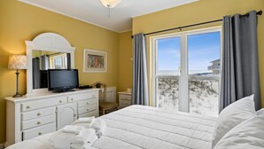 Una habitación de hotel con cama, televisión sobre una cómoda, ventana con cortinas y ventilador de techo.