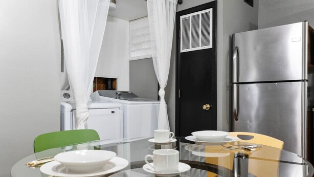 Une cuisine compacte équipée d’un réfrigérateur, d’un lave-linge et d’un four à micro-ondes. On y trouve une table en verre avec des assiettes et des tasses.