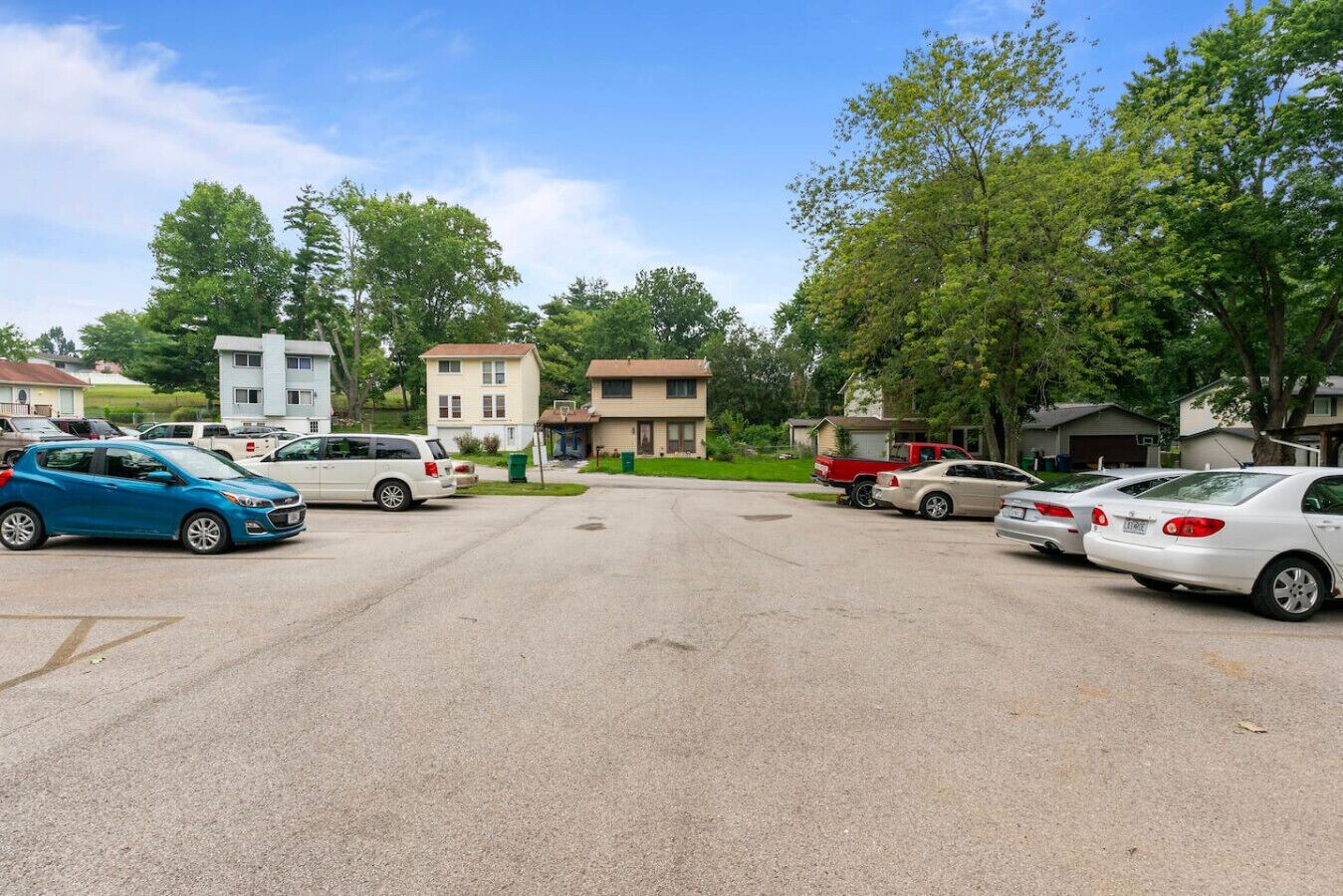 Un parking avec plusieurs voitures et des maisons en arrière-plan.