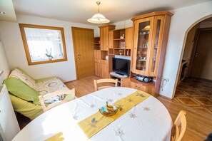 Une pièce chaleureuse comprenant un lit, une table à manger avec un chemin de table jaune, un téléviseur, des meubles en bois et une fenêtre donnant sur un beau paysage.