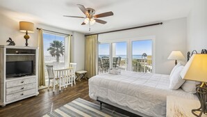 Une chambre avec un lit, une télévision, un ventilateur de plafond, une fenêtre donnant sur la plage et un balcon avec des chaises.