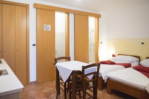 Ein Hotelzimmer mit einem Holzschrank, einem Tisch mit weißer Tischdecke und zwei Betten mit rot-weißer Bettwäsche.