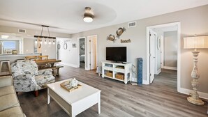 Ein geräumiges Wohnzimmer mit Holzboden, einem weißen Couchtisch, einer TV-Konsole und einem Essbereich mit Holztisch und Stühlen.