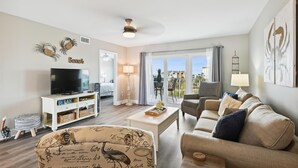 Ein Wohnzimmer mit Fernseher, Sofa und Couchtisch. Ein Balkon bietet Blick auf die Stadt.