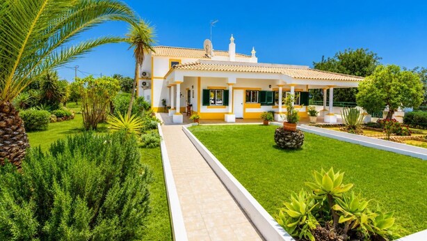 A two-story house with a tiled roof, a covered patio, and a well-maintained garden with various plants and a palm tree. - Villa Sol Nascente - Four Bedroom Villa, Sleeps 8 (Porches)
