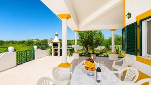 A covered outdoor seating area with a table set for dining, surrounded by white chairs, a fruit bowl, and wine glasses. - Villa Sol Nascente - Four Bedroom Villa, Sleeps 8 (Porches)