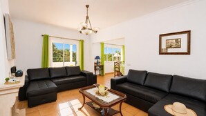 A living room with two black sofas, a wooden coffee table, and a dining area with a table and chairs. - Villa Sol Nascente - Four Bedroom Villa, Sleeps 8 (Porches)