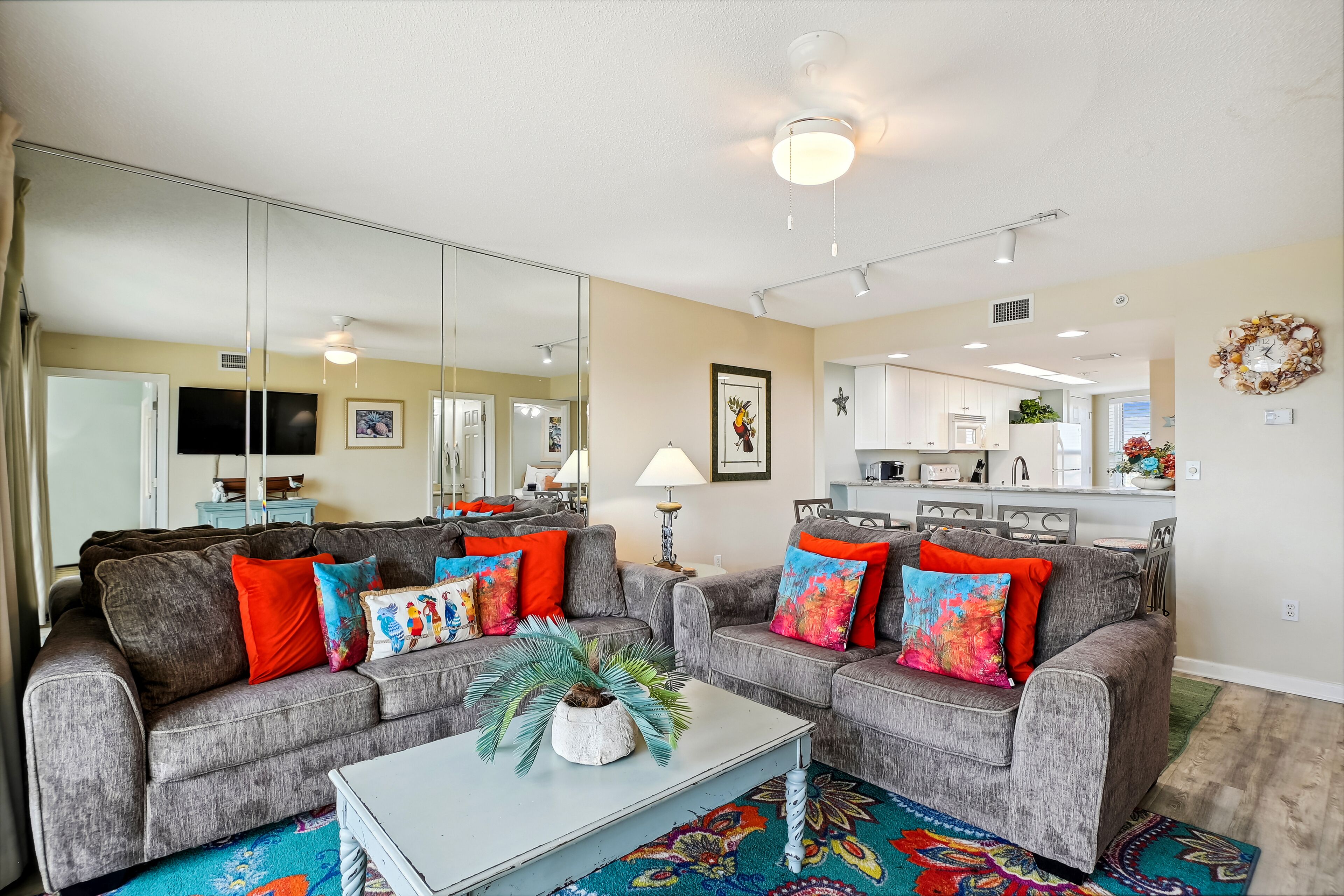 A living room with two grey sofas, colorful cushions, a white coffee table, and a large mirror.