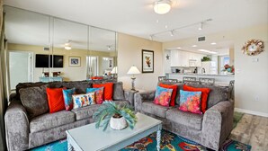 A living room with two grey sofas, colorful cushions, a white coffee table, and a large mirror. - ⛱️SeaCrest 511 - Beachfront Complex without Beachfront Prices! (Fort Walton Beach)