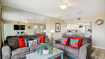 A living room with two grey sofas, colorful cushions, a white coffee table, and a large mirror.
