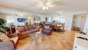 A living room with a sofa, armchair, coffee table, and dining area with chairs and a table.