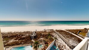 Vista para a praia a partir de uma varanda com piscina e espreguiçadeiras.