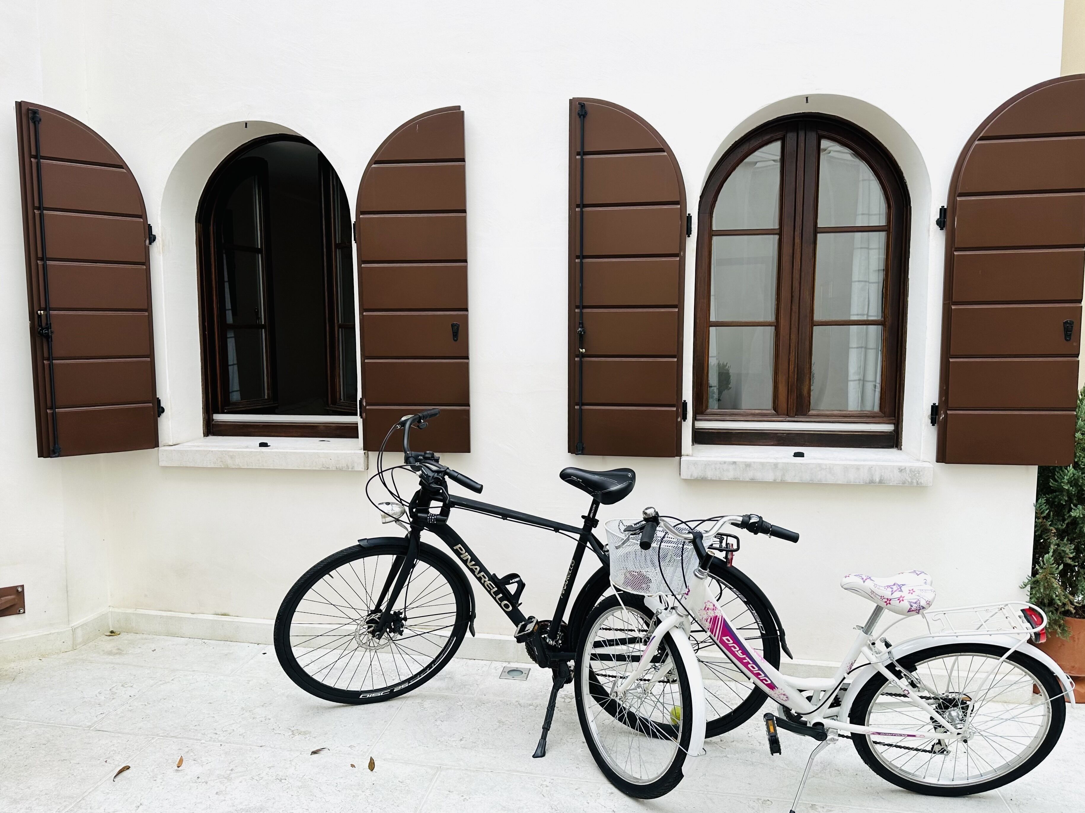 A bicycle parked in front of a building with three arched windows and brown shutters.