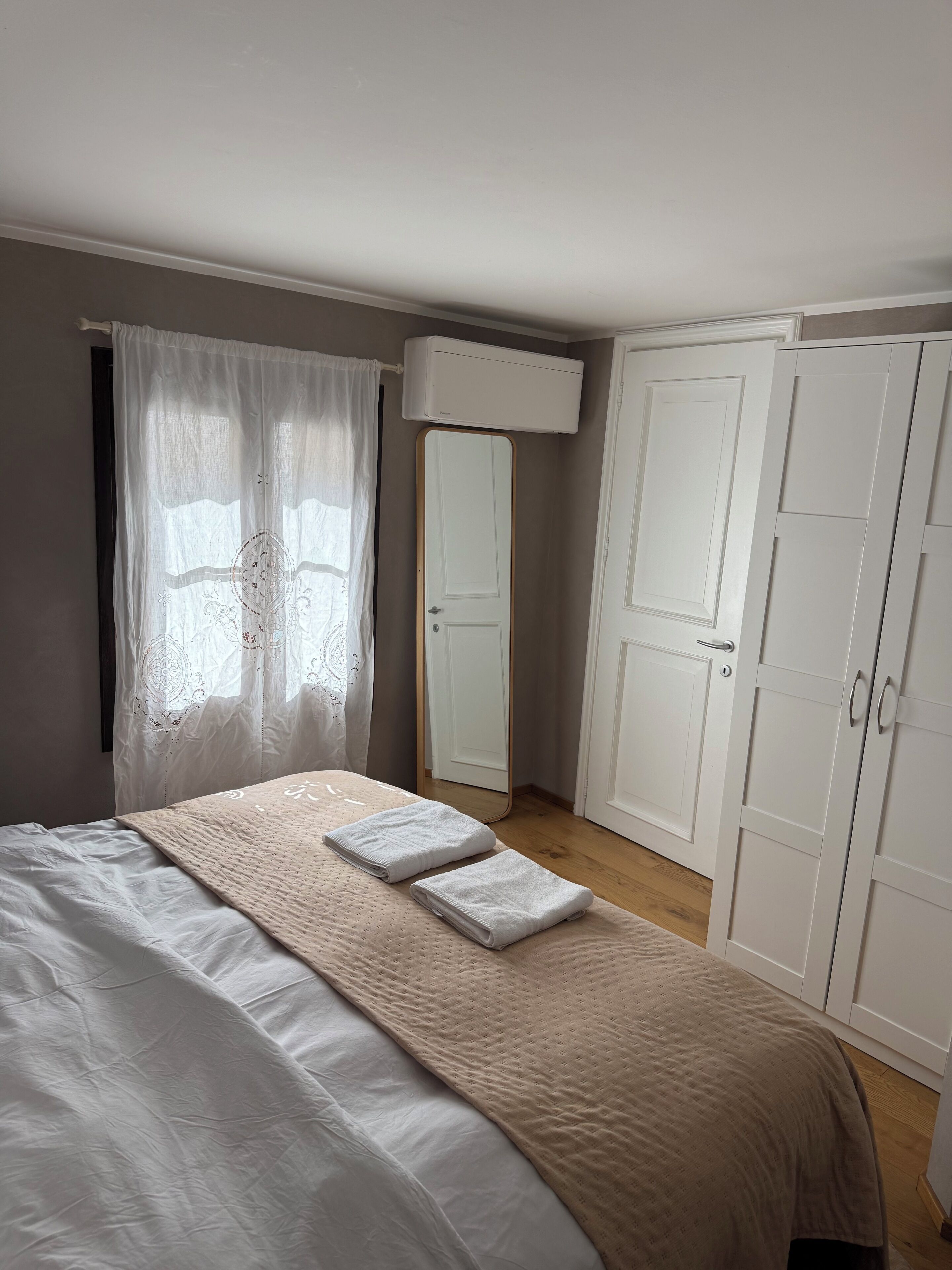 Ein Schlafzimmer mit Bett, Kleiderschrank, Spiegel und einem Fenster mit Vorhängen.