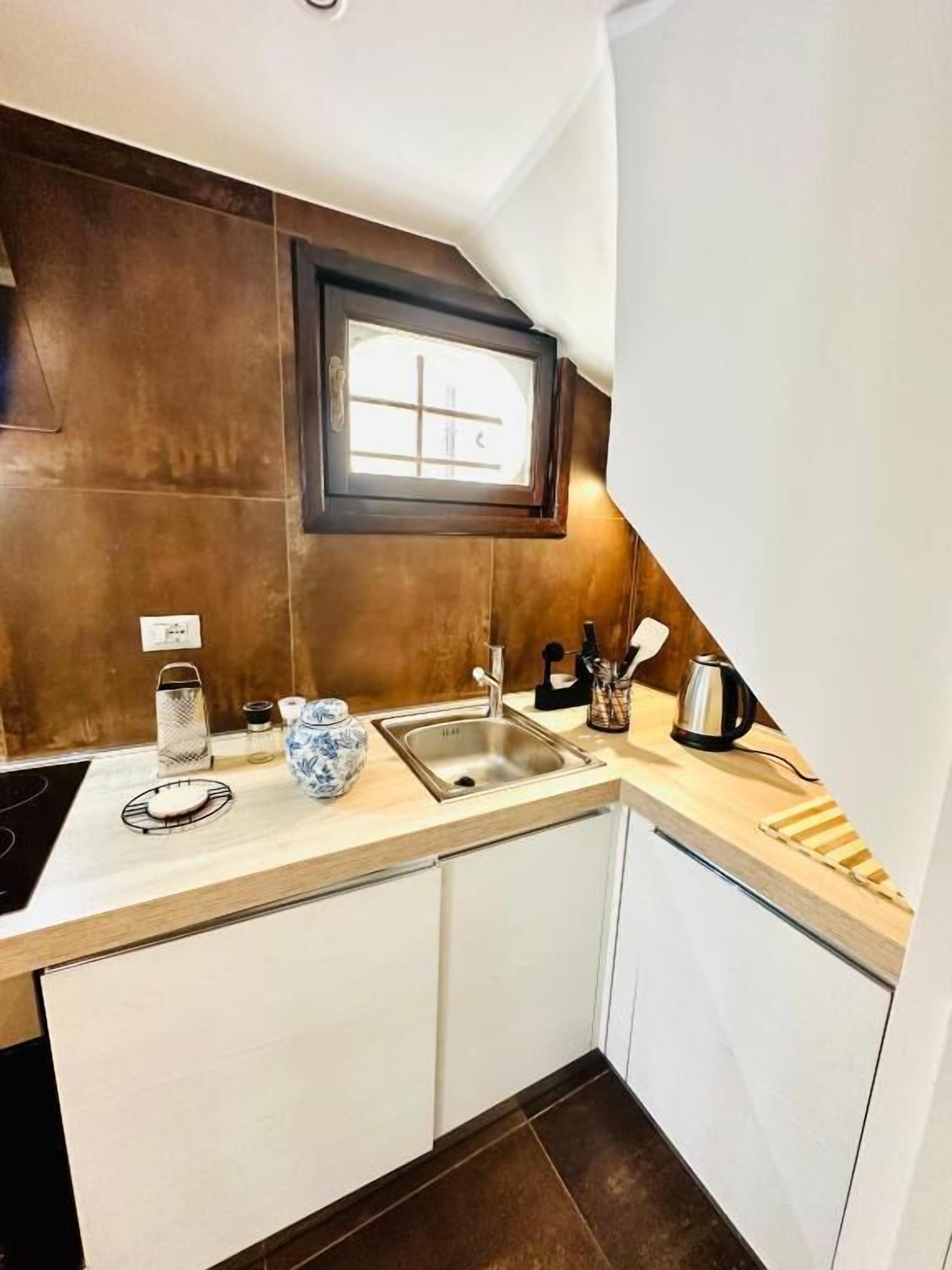 A kitchen with a sink, a window, and a countertop with a kettle and a vase.