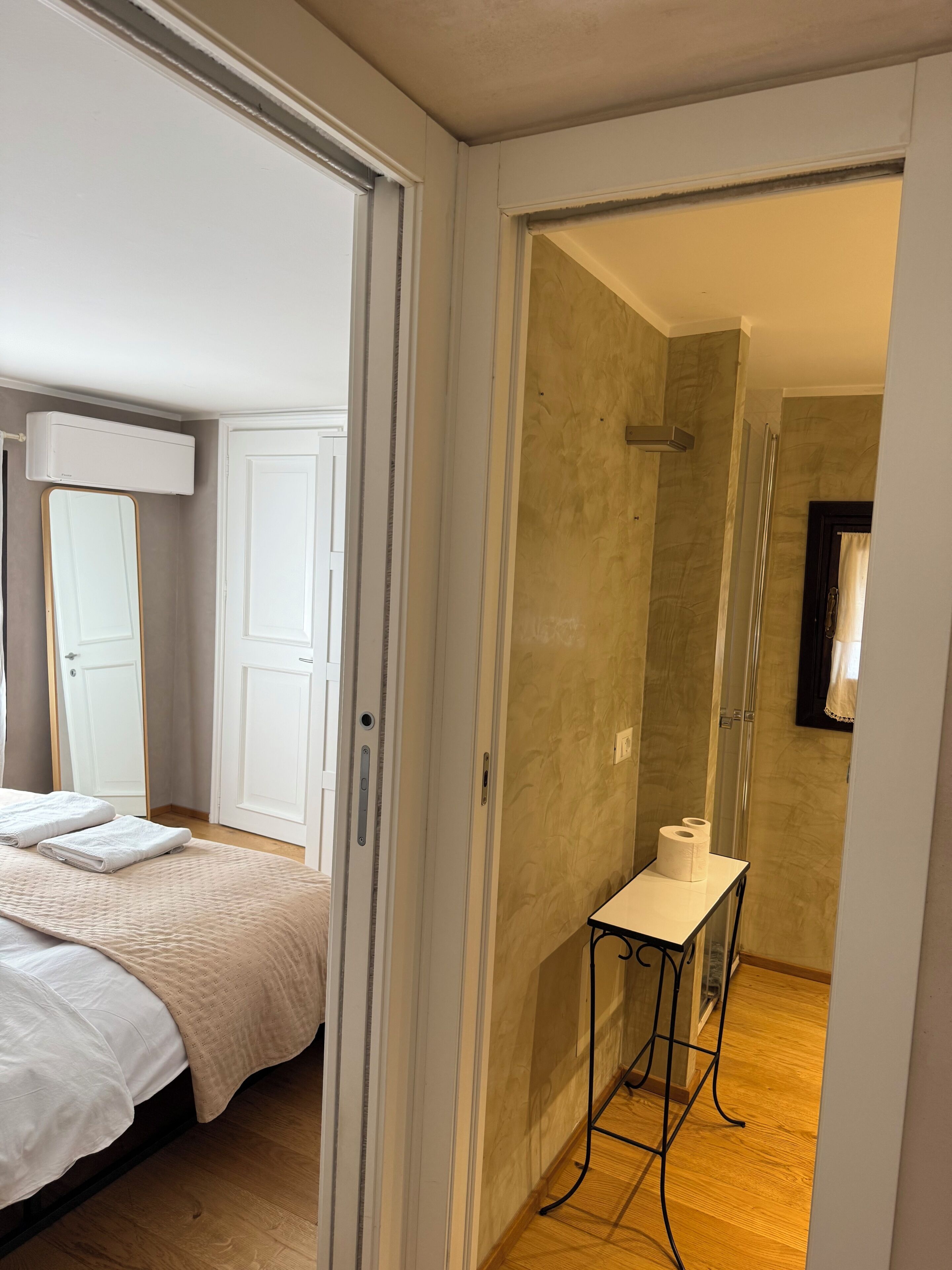 A hotel room with a bed, a bathroom with a shower, and a small table with toiletries.
