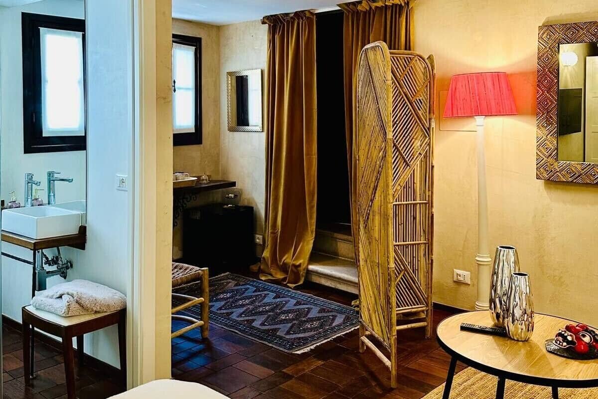 Ein Hotelzimmer mit Bett, einem kleinen Tisch mit Dekoration, einem Spiegel, einem Fenster und einem Badezimmer mit Waschbecken und Spiegel.