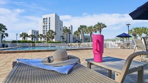 A poolside area with a lounge chair, a hat, and a pink tumbler. - Shoreline Towers 1052 - Beautiful 2 BR with Gulf views (Destin)