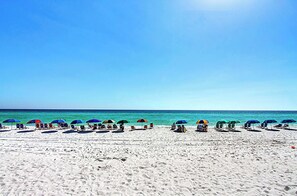 A beach with rows of sun loungers and umbrellas under a clear sky. - Shoreline Towers 1084 - Beautiful 2 BR with Gulf views and on the beach (Destin)