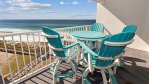 Ein Balkon mit türkisfarbenen Adirondack-Stühlen und einem kleinen Tisch, mit Blick auf Strand und Meer.