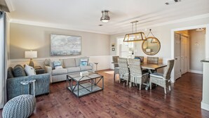 A spacious living room with a sofa, coffee table, and dining area with wicker chairs.