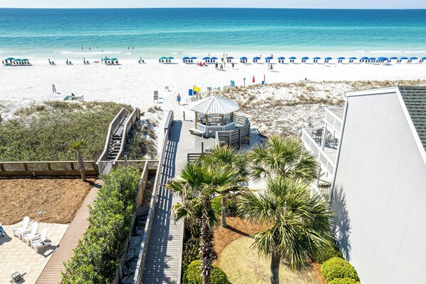 A beach view with a wooden deck, palm trees, and beach umbrellas.