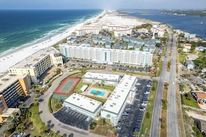 A coastal hotel with a large building, a swimming pool, and a beach view.