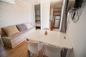 Cozy living space with a sofa, dining table, and kitchen area, featuring a geometric patterned wall and wooden floor.