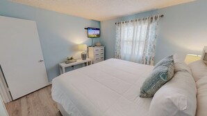 A bedroom with a bed, a TV on a stand, a dresser, a nightstand with a lamp, and a window with curtains. - Venus 308 overlooking pool Easy Beach Access (Fort Walton Beach)